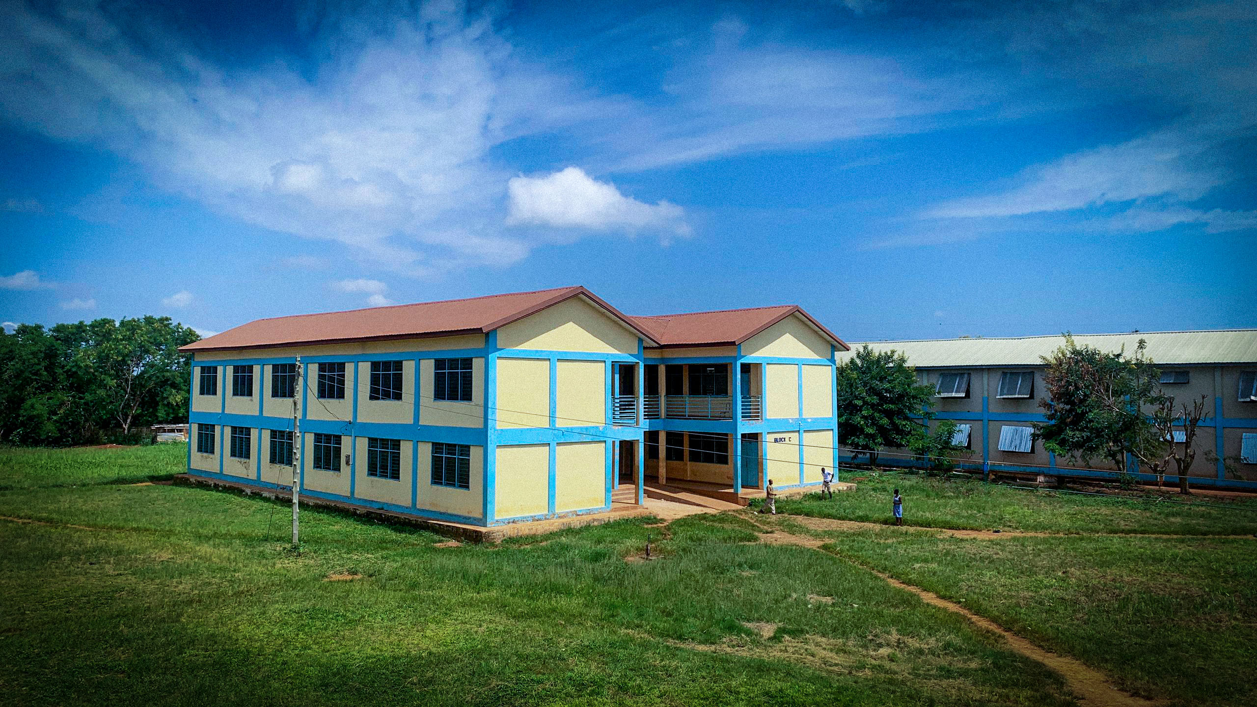 A teacher smiling at a student writing in a notebook, in a classroom setting.